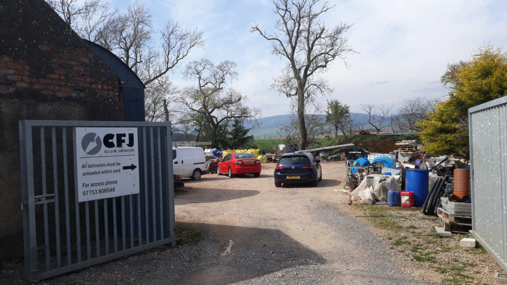 The entrance to the CFJ builders&rsquo; yard at Lower Powburn, Fordoun, with vans, materials and the hills behind